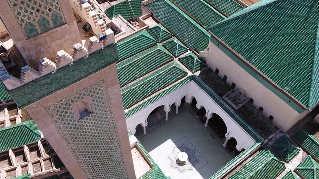 High-angle drone perspective showcasing the ornate minaret, traditional courtyard with marble fountain, and green glazed tile roofs of Al Quaraouiyine Mosque in Fez, Morocco.