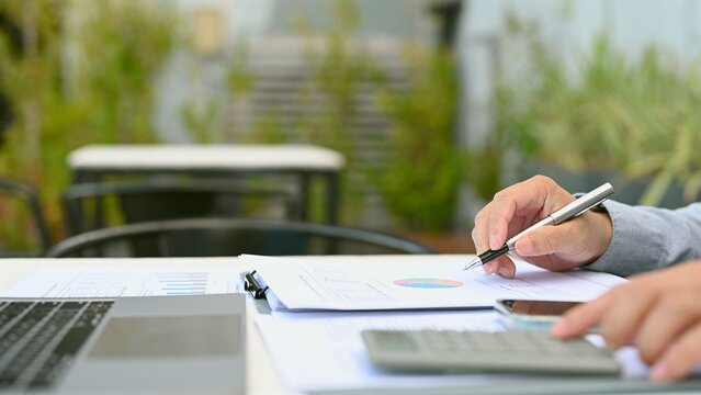 Hand holding pen conducts financial analysis, preparing budget planning, executing business data analysis, managing investment planning, completing market analysis near laptop desk.