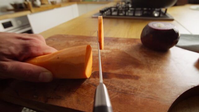 Knife point of view moves forward while slicing sweet potato on a wooden board