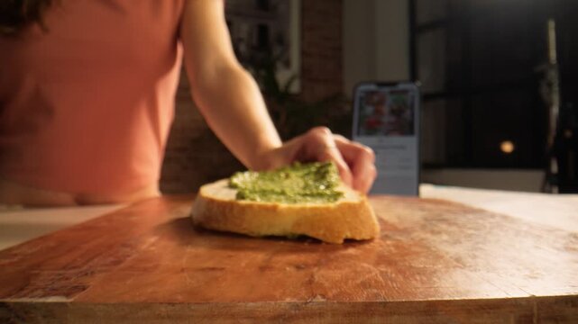 Macro closeups show a spoon spreading fresh green pesto over sliced bread