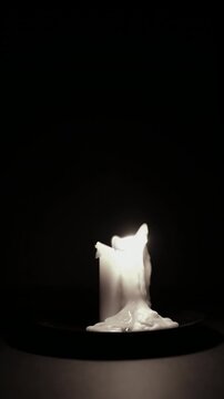 Close up shot of wax candle burning timelapse with flame glowing on wick in the dark creating mysterious scene background. Dim candle flame on black background time lapse.