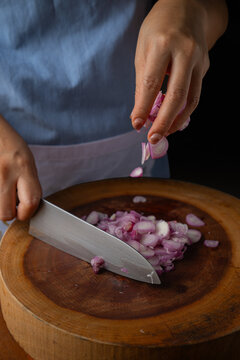 Chef dropping fresh purple shallot slices onto round wooden cutting board background.