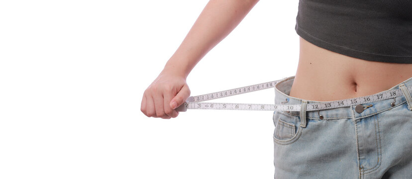 Happy slim woman showing weight loss success holding tape measure at waist line with oversized jean in modern medical concept