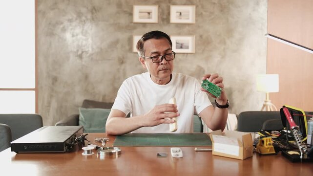 Mature Asian man checks and compares spare parts parcel, air conditioner remote control circuit board replacement, home electrical appliance fix, electronics component hobbyist, enthusiast workshop.