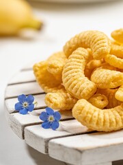 Obraz premium A delightful close-up shot of crispy golden corn puffs, beautifully piled on a rustic white wooden pallet coaster. Adorned with tiny, delicate blue flowers that add a poetic natural contrast.