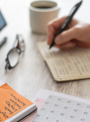 Person's hand writing notes in a notebook, managing a schedule and planning goals, tasks, and...