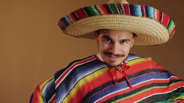 Young man wearing large woven straw sombrero with multicolored trim and bright striped woven poncho transitions from adjusting facial hair and drawstring to relaxed pose while smiling directly at