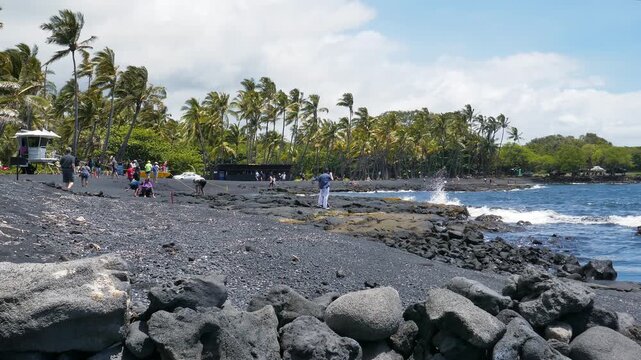Punalu'u Beach, a black sand beach located in the southern portion of the big island of Hawaii. Volcanic rocks, tourists and palm trees. Shot during early afternoon in April, 2023.