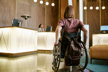 Rear view of Caucasian young adult woman with disability in wheelchair approaching hotel reception...