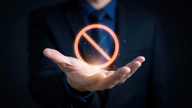 A businessman holding a glowing prohibition sign in his open palm. Restriction concept for corporate security and regulatory compliance.