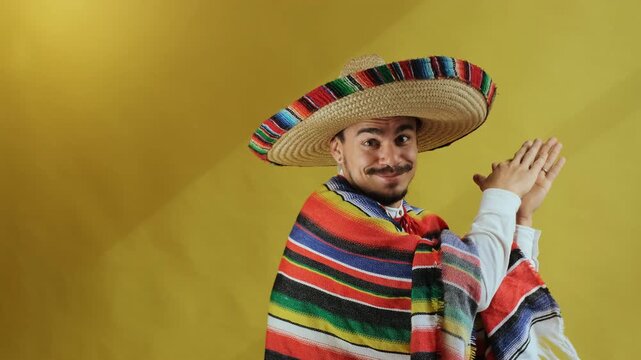 Eye-level medium-close motion of young man wearing wide-brim braided straw sombrero with multicolor embroidered brim and striped woven serape, clapping hands near chest while turning slightly toward