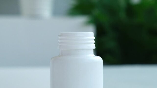 Pills falling into bottle closeup, slow motion, Green plant on background. Health, medicine and pharmaceutical concept