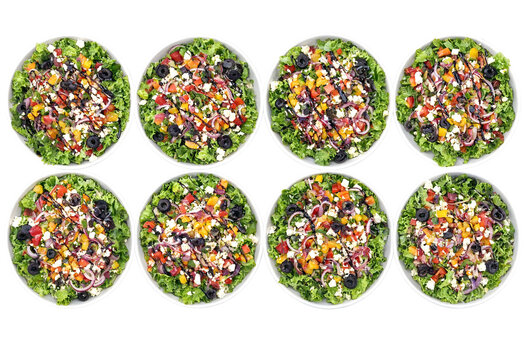 Colorful fresh greek salad with lettuce tomatoes olives peppers feta cheese and red onions in white bowls