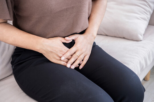 Woman holding her lower abdomen, suffering from pelvic pain, menstrual cramps, or urinary tract infection.  female experiencing health issues at home