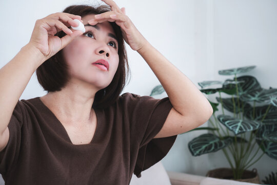 Asian woman applying eye drops bottle for dry eyes relief, irritation, or fatigue at home.  female putting artificial tears medication into her eye for vision healthcare