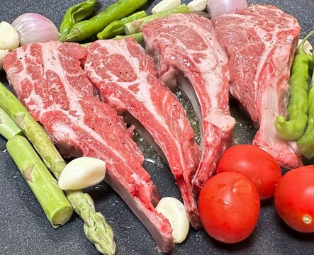 Raw lamb chops with fresh vegetables arranged on a grill pan