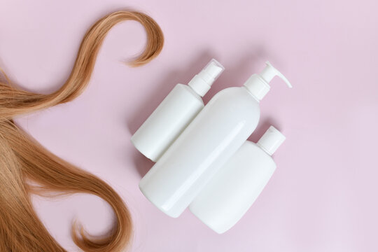 Hair strands and hair care shampoo, conditioner and hair oil product bottles on light pink background