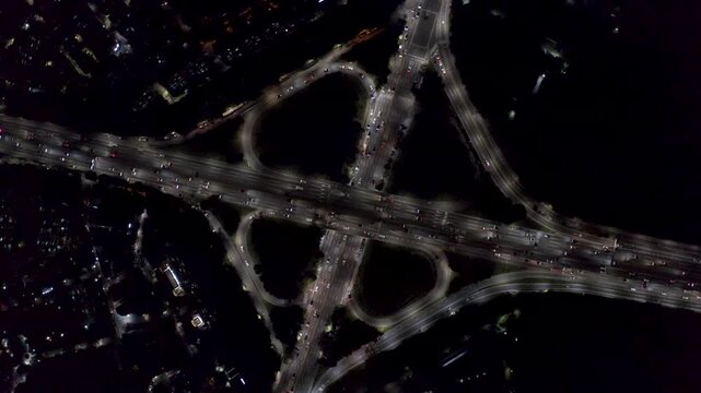 Looping ramps and multilane highways form a bright cloverleaf pattern at dark as constant vehicle streams cross in a top-down drone shot. Turcot exchange.