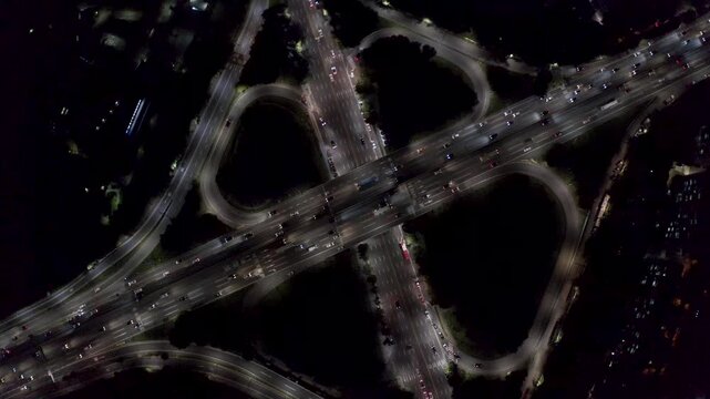 Cloverleaf freeway ramps form an X pattern as steady blue hour traffic moves through the multilevel interchange from directly above. Turcot exchange.