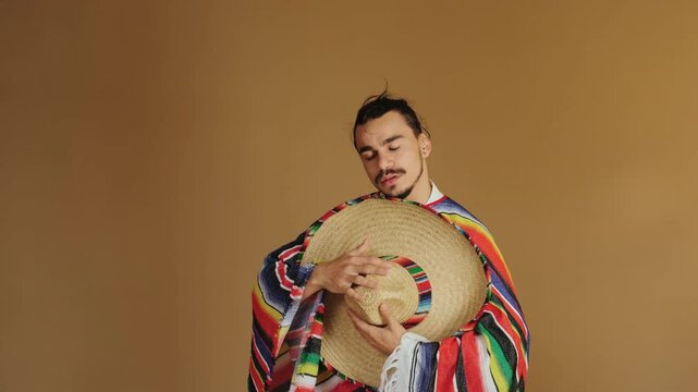 Young man turns toward camera and holds large straw sombrero at chest while shifting from concealment to presentation, eyes moving from closed to direct subtle gaze and expression moving from