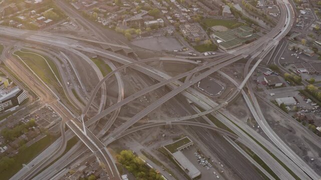 Curving ramps of the Turcot Interchange cross rail yards and work zones in soft evening light as the camera glides overhead.