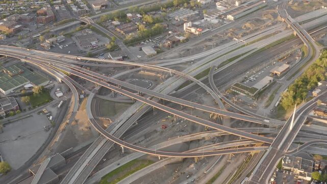 Curved ramps of the Turcot Interchange cross active rail lines and work zones in soft evening light from a high drone pass.