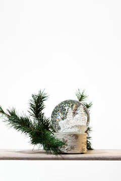 Shimmering gold Christmas ornaments in a rustic cardboard organizer paired with green pine branches. A vertical minimalist composition perfect for holiday sales and sustainable winter decor themes.