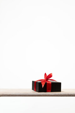 Sleek matte black present with a decorative crimson bow resting on a wooden surface. Ideal for minimalist aesthetic marketing, Valentine's Day offers, and sophisticated corporate gifting campaigns.