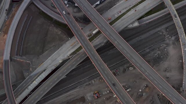 Multiple stacked highway ramps cross active rail tracks and construction yards in a geometric top-down aerial shot.