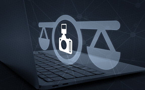 Legal photography and media law concept illustration with a digital camera icon inside scales of justice floating above a modern laptop computer keyboard.