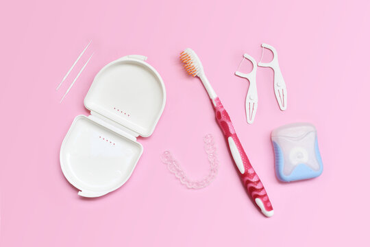 Top view of dental clear aligners, toothbrush, toothpicks and floss on pink background with copy space