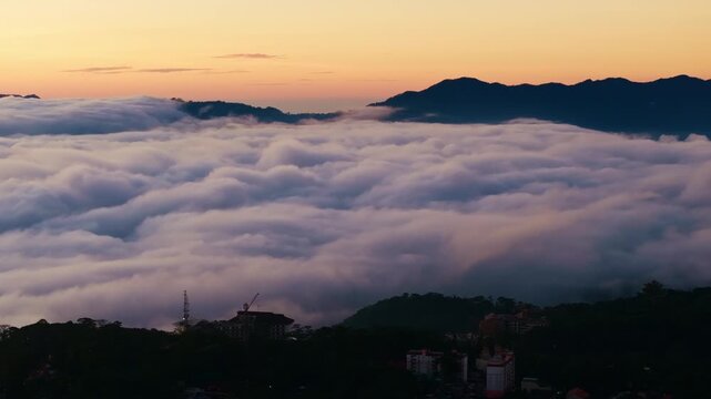 Drone pans left above soft clouds glowing at sunrise over Benguet mountains