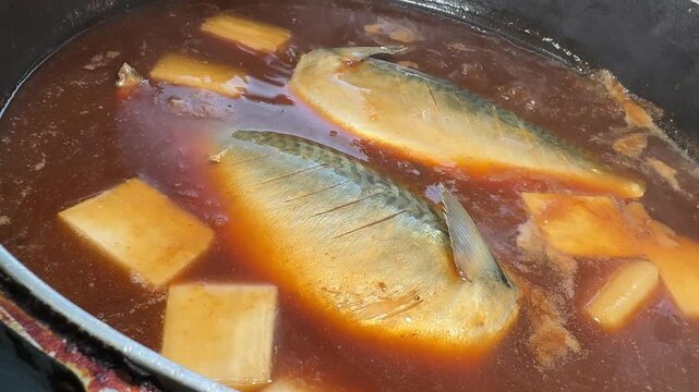 Ladling miso broth over simmering mackerel, saba no misoni in a pan at an izakaya kitchen in Japan