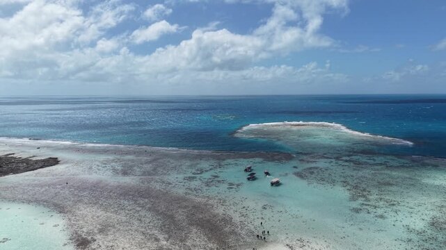 Aerial drone shot descending over tour boats anchored in the shallow turquoise water near the outer reef boundary of the Blue Lagoon in Rangiroa