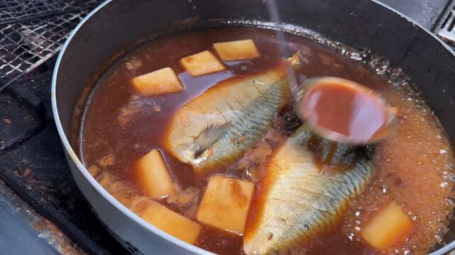 Saba no Misoni, mackerel simmered in miso, chef ladling hot miso broth over the fish in a pan at an izakaya kitchen in Japan