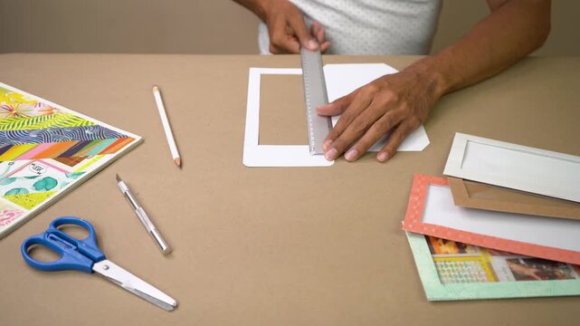 Hands measuring and cutting cardstock with ruler and craft tools on work table