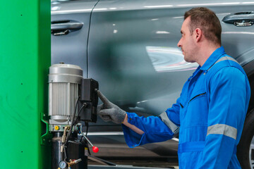Naklejka premium Male mechanic in blue coveralls working under car raised on hydraulic lift in auto repair garage
