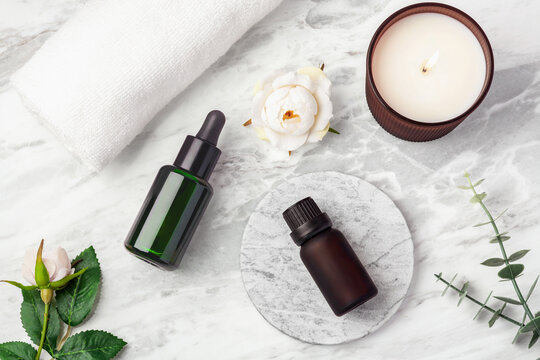Essential oil bottle, scented candle, white towel, and pink rose flowers on marble background.