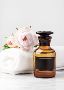 Aromatherapy essential oil bottles with blank black label, pink roses and towel on white marble table, closeup