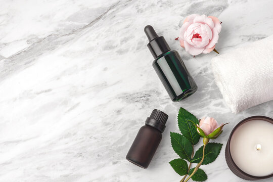 Essential oil bottles, pink rose,  towe andl burning candle on marble table background, copy space