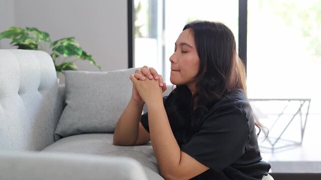 Asian woman praying at home, folded hands in prayer feel grateful, meditating with her eyes closed, praying to request God for help