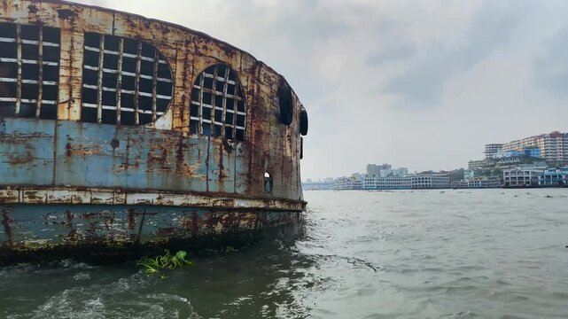 The rear of a cargo ship is visible on the Buriganga River in Dhaka, Bangladesh, showing inland waterway transport on the river beside the city