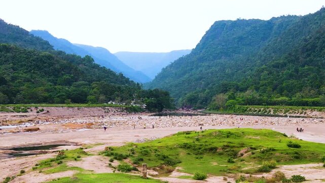 Panning drone shot of a huge dry river bed and the Khasi hills near the Bangladeshi and and Indian border, as tourists enjoy the beautiful wild landscape and impressive rolling hills