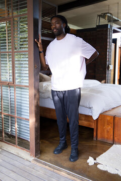 African-American male standing in bedroom doorway to deck, bed, wearing white tee, wristwatch