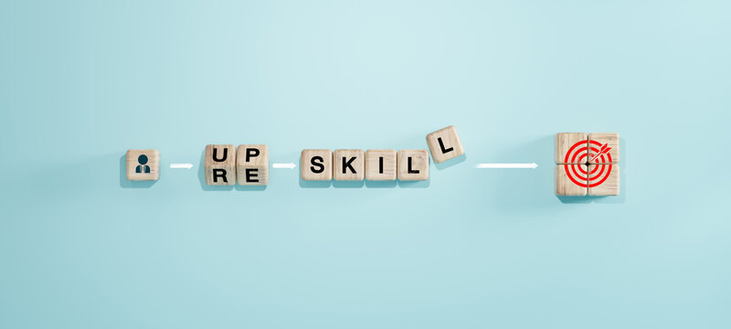 Wooden blocks with Upskill Reskill text connecting person icon to target goal, employee professional development and training concept.