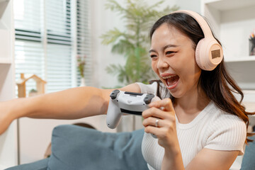 Young woman wearing wireless headphones while playing video games with a game controller at home. Excited gamer enjoying online gaming, entertainment, competition and modern digital lifestyle. © Imagestoyou