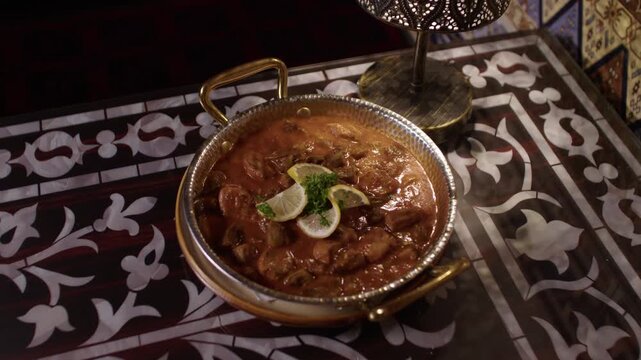 Traditional Turkish stew served in a metal dish on an ornate patterned table indoors