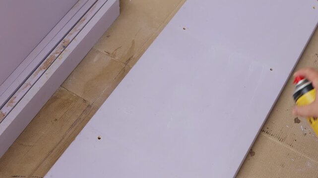 Close-up shot of applying aerosol paint stripper on old painted wood preparing for refinishing. Ideal for DIY home improvement tutorials, furniture restoration guides, woodwork repair videos, and reno