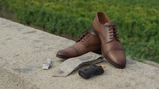 Brown leather groom shoes wristwatch tie and perfume bottle on stone wall outdoors