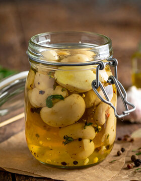 Traditional homemade pickled mushrooms with garlic preserved in glass jar, savory brine with herbs and spices, rustic wooden table, freshly prepared winter preserves, close-up.
